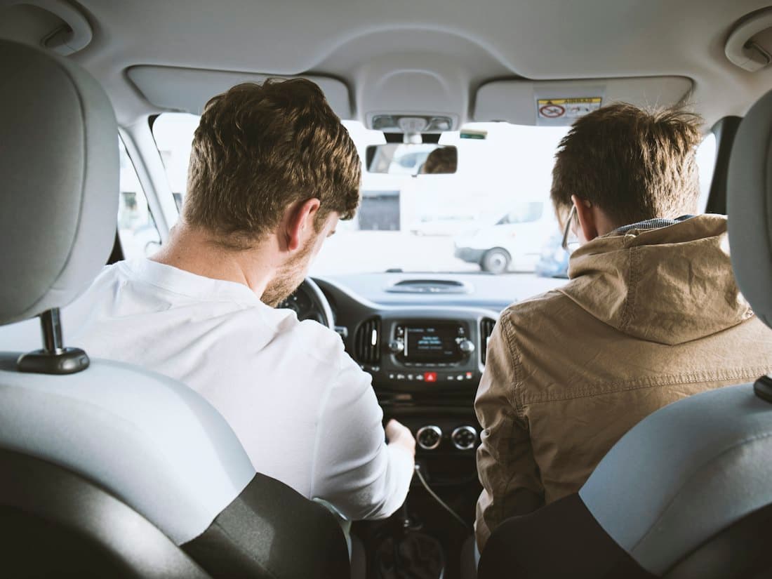 An instructor sitting beside a learner driver during a lesson, viewed from the rear seats