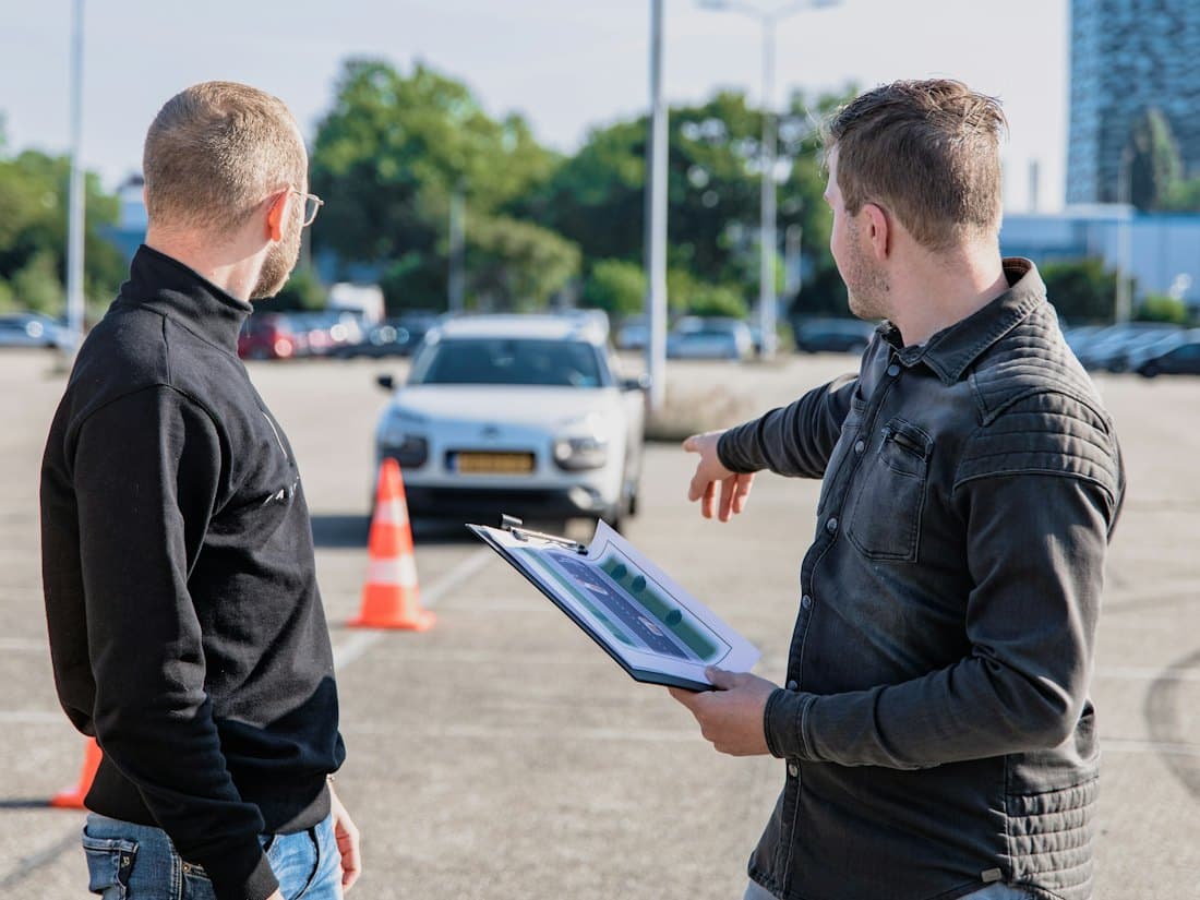 An examiner with a clipboard beside a test car and cones
